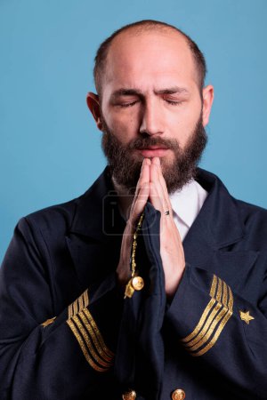 Photo for Airline pilot in uniform praying to gods with closed eyes, standing with folded hands gesture. Religious middle aged plane captain pleasing, aviator worshiping before flight, praising - Royalty Free Image