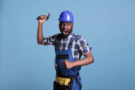 Photo for Angry strong african american construction worker in fighting stance with aggressive facial expression holding hammer in front of camera. Worker in attack position with aggressiveness in studio shot. - Royalty Free Image