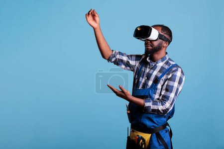 Téléchargez les photos : African american builder wearing virtual reality goggles in a simulation of new renovation project. Master builder working on new construction techniques using 3d technology. - en image libre de droit