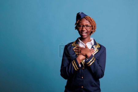 Photo for Happily smiling african american stewardess lady portrait. Female flight worker looking surprised, expectant, glad at camera. Suit dressed lucky woman laughing on blue background. - Royalty Free Image