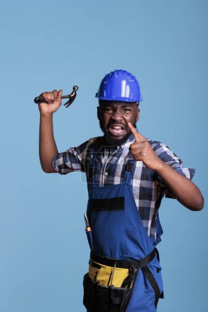 Foto de Angry construction worker angry and upset about overwork and long hours without rest. Frustrated upset person shouting aggressively while having an argument with employer against blue background. - Imagen libre de derechos