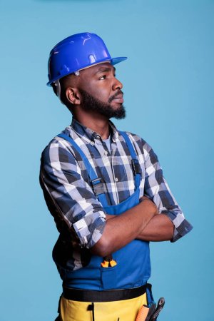 Photo for African american builder detailing the work he has just completed on the installation of electrical wiring to light the roof. Electrician wearing coveralls hard hat in studio shot. - Royalty Free Image