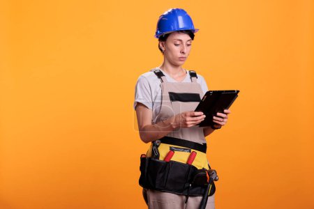 Téléchargez les photos : Portrait of woman industry engineer working with tablet, looking for renovating inspiration online on wireless gadget. Female contractor in overalls using electronic digital device. - en image libre de droit