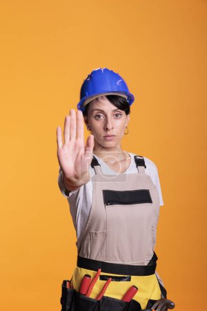 Foto de Female construction worker disapproving idea, raising palm to show refusal and decline suggestion. Serious female builder doing stop sign and expressing rejection and denial in studio. - Imagen libre de derechos