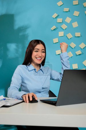 Téléchargez les photos : Optimistic asian woman receiving a promotion at work, excited while reading notification email on laptop. Female businesswoman smiling excitedly at contemporary workplace. - en image libre de droit