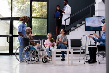 Photo for Physician nurse discussing medical diagnosis with family explaining health care treatment during checkup visit in hospital reception. Elderly woman in wheelchair finising consultation - Royalty Free Image