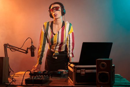 Photo for Flirty disc jockey acting silly with tongue out, fooling around in studio with lights. Playful funky woman mixing techno music with mixer or turntables, being confident and laid back. - Royalty Free Image