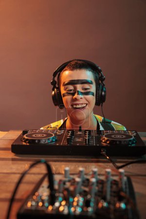 Téléchargez les photos : Young performer looking at dj turntables in studio, preparing to mix techno music and have fun at nightclub. Woman with crazy make up watching mixer on table, look closely and acting silly. - en image libre de droit