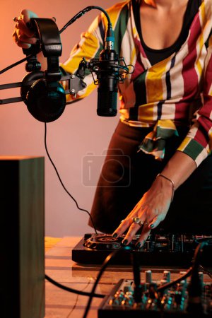 Téléchargez les photos : Woman musician using dj equipment and headphones to mix techno music and play electric remix on turntables, having fun with stereo instrument used for mixing sounds, bass volume. - en image libre de droit