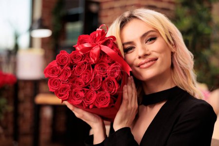 Téléchargez les photos : Cute girlfriend posing with valentines day red roses bouquet, receiving romantic gift from boyfriend during love holdiday. Attractive woman smiling at camera, holding flowers in heart shaped box - en image libre de droit
