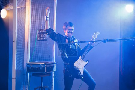 Foto de Crazy artist performing live show in studio, playing electric guitar and singing heavy metal music. Cool funky singer doing alternative rock performance with leather jacket and dark make up. - Imagen libre de derechos