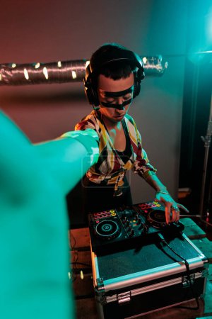 Foto de Female DJ with cool makeup mixing techno music, using turntables to produce remix of record in studio with colorful lights. Disc jockey performing at club with stereo and audio equipment. - Imagen libre de derechos