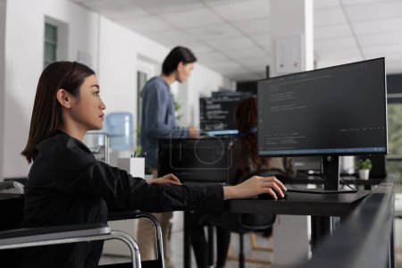 Foto de Web developer in wheelchair working on server coding in big data office, analyzing programming language and script on terminal window. Disabled woman programmer with impairment working on it system. - Imagen libre de derechos