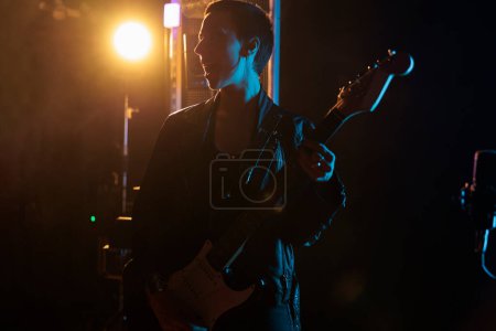 Photo for Rockstar woman with leather jacket holding electric guitar while performing heavy metal song, working at rock album in studio. Musician person playing punk music, adjusting electricinstrument - Royalty Free Image