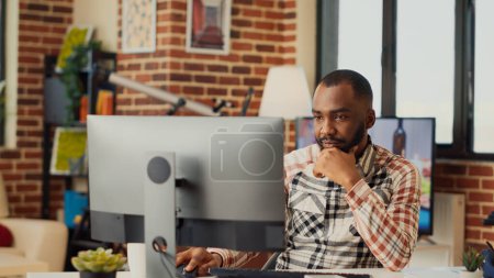 Photo for African american man working from home on computer, analyzing financial sales report online. Young worker doing remote job on company network, checking email and accounting result. - Royalty Free Image