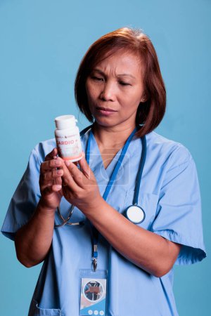 Foto de Serious medical assistant working at medication treatment to prevent patient sickness, holding drugs box reading pharmaceutical leaflet in studio with blue background. Health care service and concept - Imagen libre de derechos