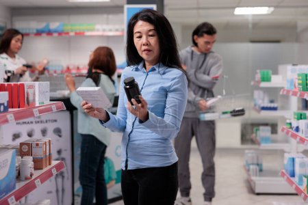 Téléchargez les photos : Adult customer looking at bottles of pills to buy prescription treatment from pharmacy shelves, pharmaceutical supplies. Asian woman examining medical products in packages to cure disease. - en image libre de droit