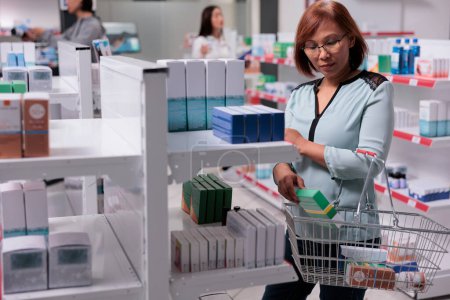 Téléchargez les photos : Asian woman examining vitamins box on shelves, looking to buy medical supplements and pharmaceutical products. Checking package of healthcare supplies and medicaments in pharmacy shop. - en image libre de droit
