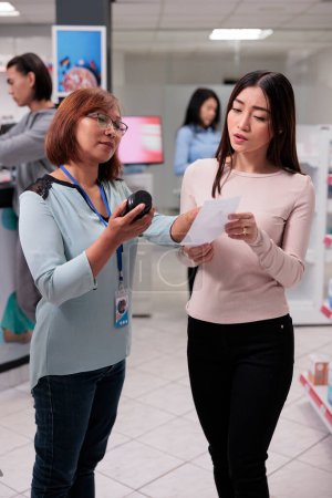 Téléchargez les photos : Asian specialist reading prescription paper in pharmacy shop to give medicaments and supplements to customer. Female client buying medication, drugs or capsules boxes from pharmaceutical drugstore. - en image libre de droit