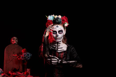 Photo for Spooky lady of dead with flowers headband posing in studio as holy santa muerte and la cavalera catrina. Young woman acting glamorous with black and white costume, day of the dead tradition. - Royalty Free Image