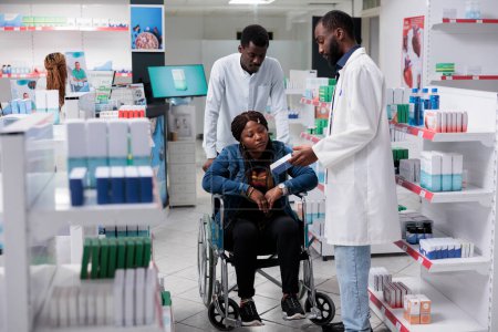 Téléchargez les photos : African american woman with disability shopping in drugstore, pharmacist recommending medicaments. Medications retail, client and pharmacy store consultant talking, all black team - en image libre de droit