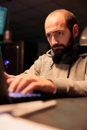 Foto de Male hacker using computer to break into corporate data servers and infect software system with dangerous virus. Scammer working at night to steal information, security breach malware. - Imagen libre de derechos