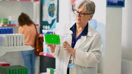 Photo for Woman pharmacist holding box of pills with greenscreen, working in pharmacy shop. Specialist looking at isolated chroma key background with mockup blank template, package of medicaments. - Royalty Free Image