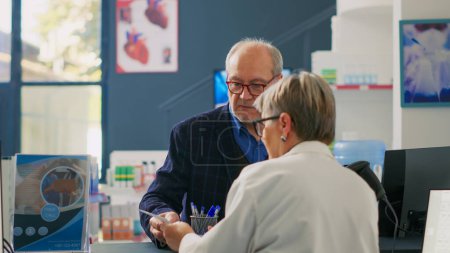 Photo for Health specialist helping senior client with prescription paper, finding pills and supplements for disease treatment. Elderly man looking for medicaments at pharmacy counter, cash register. - Royalty Free Image