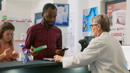 Photo for Diverse people buying pharmaceutical products at cash register, paying with smartwatch, mobile phone with nfc and credit card. Customers having pills and medicaments at counter. - Royalty Free Image