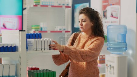 Téléchargez les photos : Woman examining drugstore shelves with pharmaceutical products, looking for prescription treatment to buy medicaments. Female client checking pills and boxes at pharmacy. Handheld shot. - en image libre de droit