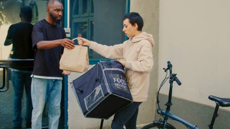 Photo for Confused courier delivering wrong fastfood order to client, unsatisfied man acting displeased about restaurant takeaway problem. Food delivery service worker with backpack on bicycle. - Royalty Free Image