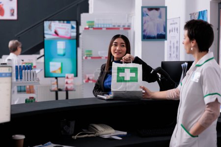 Téléchargez les photos : Femme prenant des médicaments acheter un sac à provisions au comptoir de la pharmacie, l'achat de produits pharmaceutiques en pharmacie. Apothicary caissier vente de jeunes médicaments asiatiques à la caisse - en image libre de droit