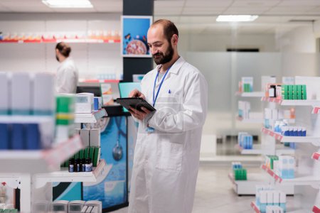 Foto de Drugstore worker holding tablet computer checking client prescription while preparing pills order. Pharmacy maintains an inventory of all the different types of medicine and medical supplies in stock. - Imagen libre de derechos