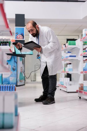 Photo for Pharmacist looking at medical pills information on tablet computer while scanning drugs barcode using pharmacy scanner. Drugstore employee is responsible for organizing and labeling packages - Royalty Free Image