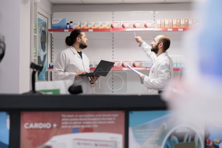 Foto de Two men pharmacists doing medicaments inventory checking drugs packages, typing vitamins information on laptop. Pharmacy is a reliable and convenient location for filling prescription medication - Imagen libre de derechos