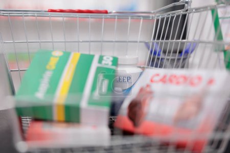 Foto de Store shopping basket filled with medicaments and medical products standing on counter desk in drugstore. Pharmacy offered a wide selection of vitamin and supplement drugs in individual packages. - Imagen libre de derechos