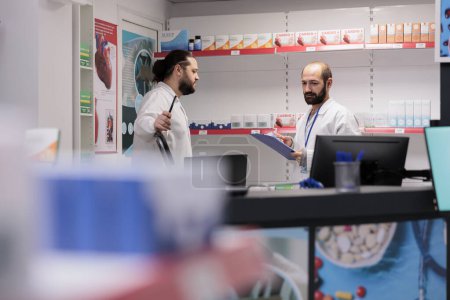 Foto de Drugstore workers in white coat maintains an inventory of all the different types of medication and medical supplies in stock in pharmacy, writing drugs info. Health care support service and concept - Imagen libre de derechos