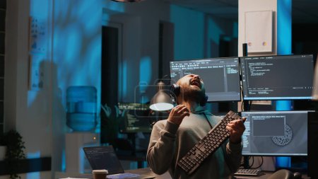 Photo for Careless html coder playing air guitar with keyboard, having fun and acting silly after hours. IT engineer fooling around with instrument and enjoying late night working in office, happy man. - Royalty Free Image