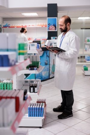 Téléchargez les photos : Pharmacist looking at pills packages typing inventory information on tablet computer in drugstore. Pharmacy is a trusted source for high-quality and effective medication and treatment options. - en image libre de droit