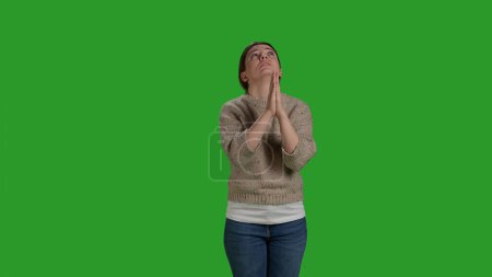 Téléchargez les photos : Vue de face du modèle féminin priant Dieu à la caméra, tenant les mains de prière et mendiant pour bonne chance. Femme religieuse exprimant espoir et croyance, demandant fortune sur écran vert. Gros plan. - en image libre de droit