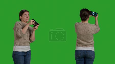 Photo for Happy modern person playing videogames online on smartphone, using mobile phone to have fun with gaming competition on internet app. Woman enjoying play on telephone, greenscreen studio. - Royalty Free Image