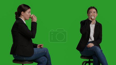 Photo for Close up of corporate employee serving coffee cup in studio, drinking caffeine beverage and sitting on chair. Businesswoman enjoying refreshment and drink wearing formal office suit. - Royalty Free Image