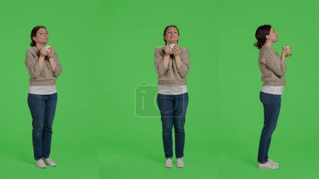 Photo for Caucasian girl drinking cup of coffee over full body greenscreen background, holding caffeine drink in studio. Young woman enjoying caffeine beverage on isolated greenscreen, portrait. - Royalty Free Image