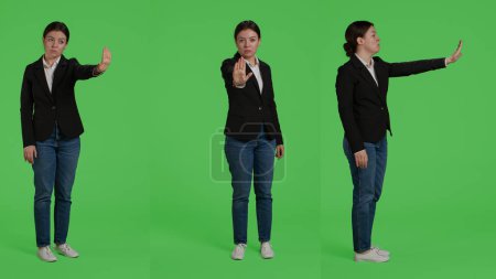 Photo for Businesswoman doing no sign with palm on camera, expressing disapproval and denial. Young adult in suit showing rejection and refusal gesture over full body greenscreen backdrop. - Royalty Free Image