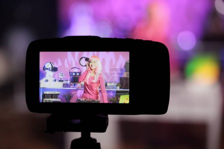 Téléchargez les photos : Artiste asiatique interprétant une chanson électronique sur des platines professionnelles en s'amusant tout en enregistrant une session de musique avec caméra. Dj avec cheveux roses faisant des performances à la boîte de nuit avec équipement audio - en image libre de droit