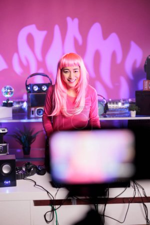 Téléchargez les photos : Dj aux cheveux roses interprétant une chanson électronique sur des platines tournantes professionnelles tout en enregistrant une session musicale avec caméra, en s'amusant en club pendant la nuit. Danse d'artiste tout en jouant remix techno - en image libre de droit