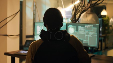 Téléchargez les photos : Silhouette of male hacker breaking firewall encryption to plant trojan virus, looking to steal valuable data late at night. Young thief using computer malware to hack online web system. - en image libre de droit