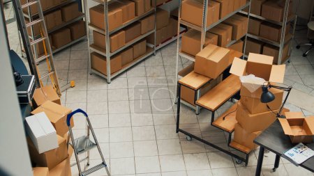 Foto de Empty storehouse space with stacks of cardboard boxes, small business concept with shelves and racks of stock merchandise. Products packed in packages used for shipment and delivery. - Imagen libre de derechos