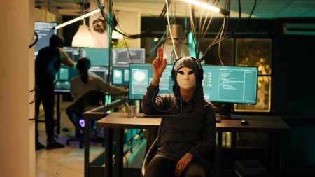 Téléchargez les photos : Pirate anonyme avec masque utilisant l'hologramme pour pirater le serveur informatique et voler des informations. Espion masqué travaillant avec des données holographiques pour le cryptojacking et l'espionnage, réalité augmentée. - en image libre de droit