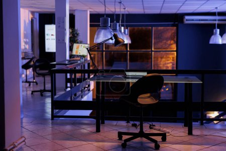 Intérieur du bureau d'affaires vide avec des meubles modernes pendant la nuit, ayant rapport graphique financier en cours d'exécution sur l'écran de l'ordinateur. Entreprise de marketing avec personne dedans, lieu de travail start-up